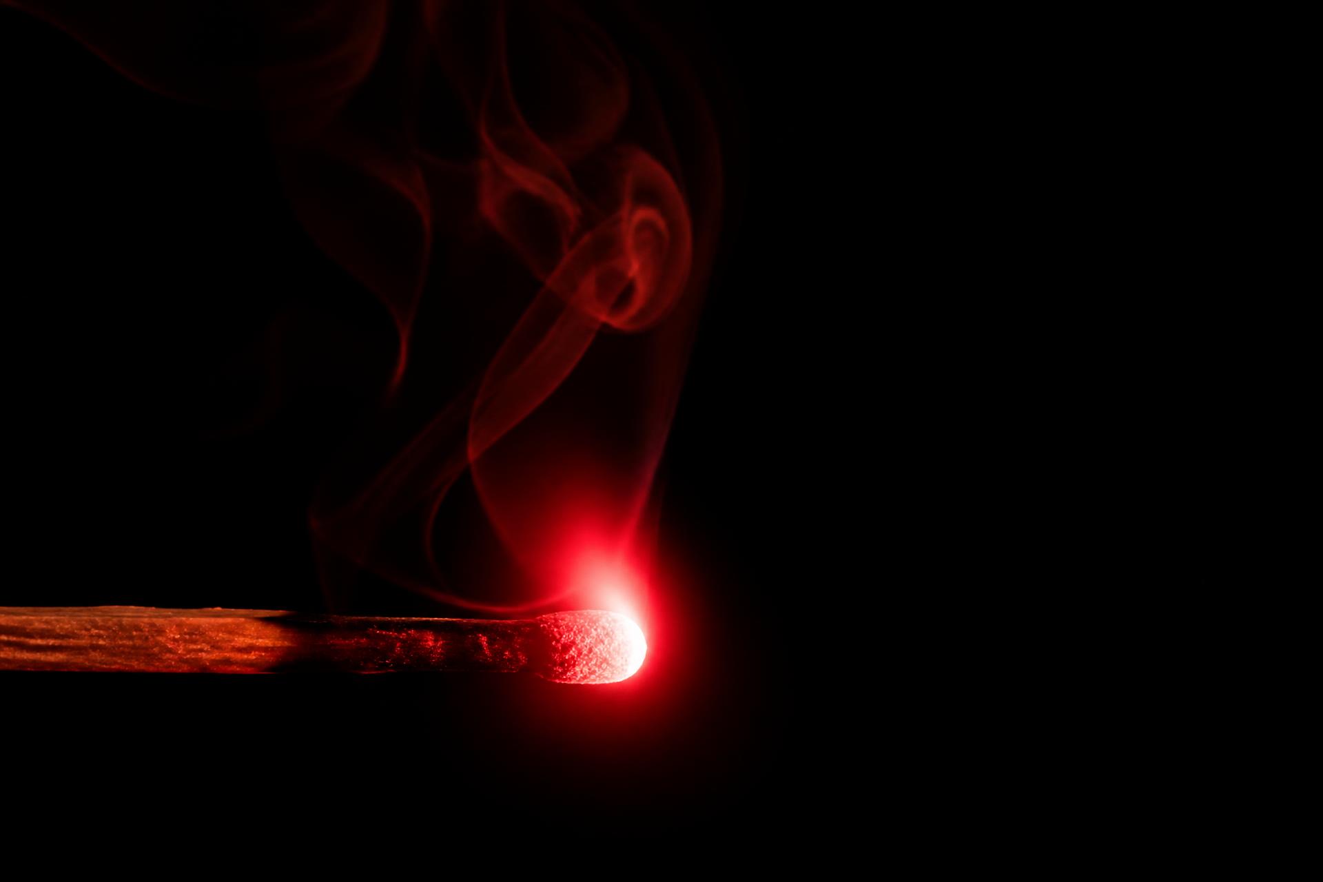a match head flaring red in near total darkness